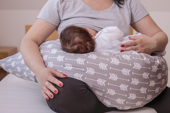 A mother breastfeeding a child that is placed on a large pillow on her lap