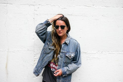 A woman posing with her hand running through her hair in a denim jacket