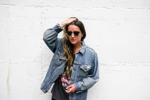 A woman posing with her hand running through her hair in a denim jacket