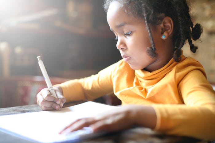 A little girl in an orange shirt who has back-to-school anxiety writing something
