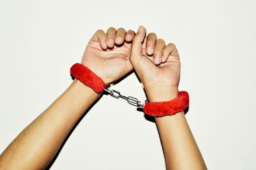 Fuzzy red handcuffs on hands.