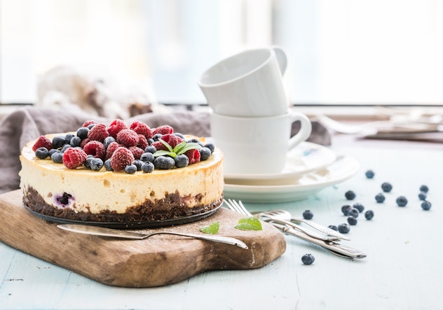 A cheesecake with berries on top, two empty coffee cups are in the background