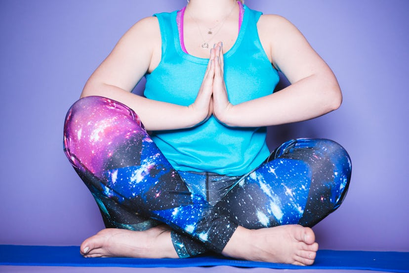 A woman is meditating in pink, blue and red leggings and top