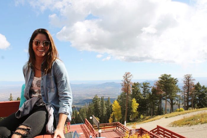 Alyssa Himmel wearing a denim jacket and black jeans, smiling while posing on a mountain terrace.