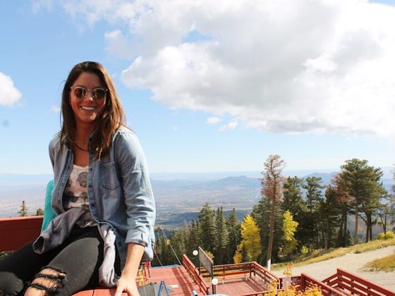 Alyssa Himmel wearing a denim jacket and black jeans, smiling while posing on a mountain terrace.