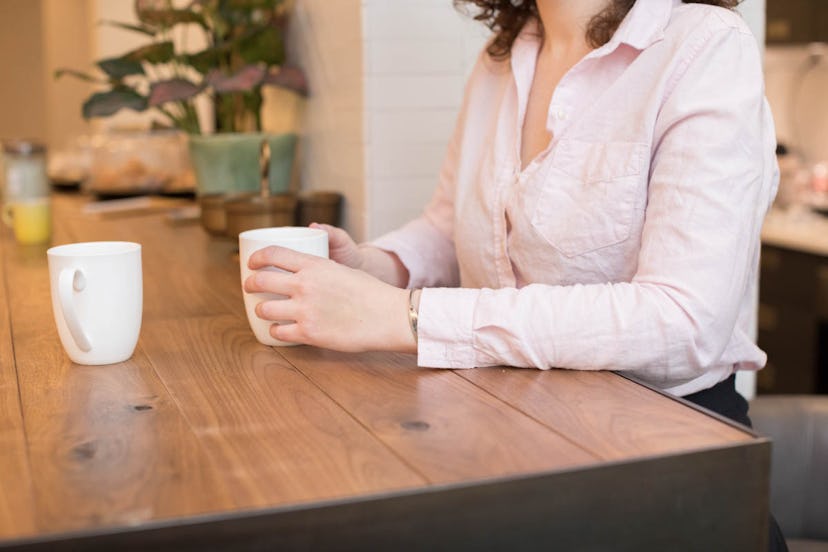 Woman in a white button-up holding a cup of coffee at a coffee shop