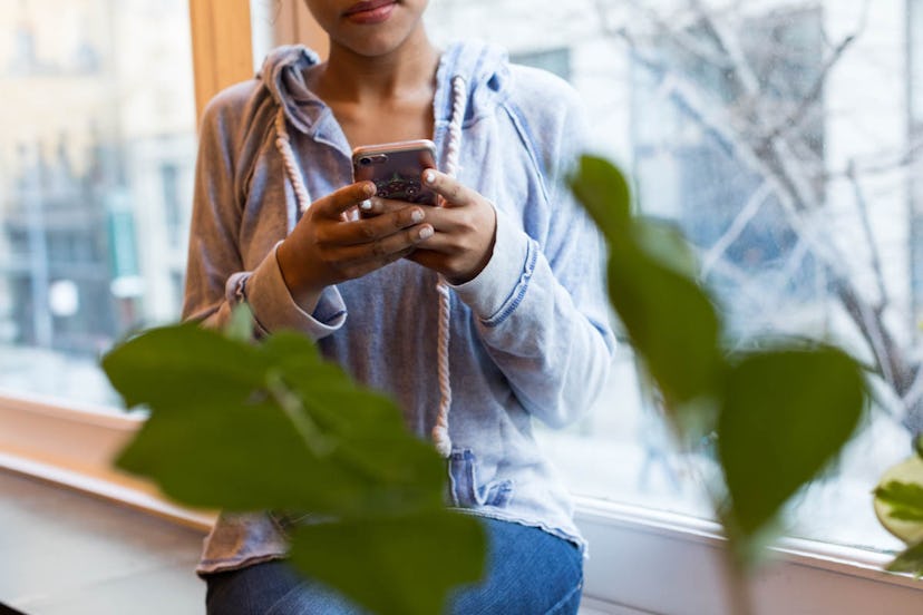 A girl standing next to a window and using her smartphone to plan an STI testing appointment