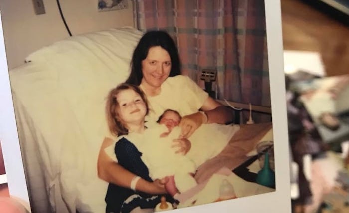 A mother posing in a hospital bed with her toddler daughter and newborn baby
