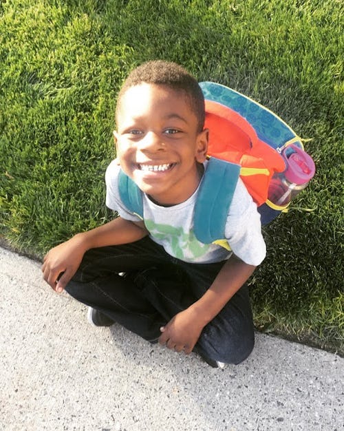 A smiling, happy child with a backpack, whose mom has back-to-school anxiety that white moms just ca...