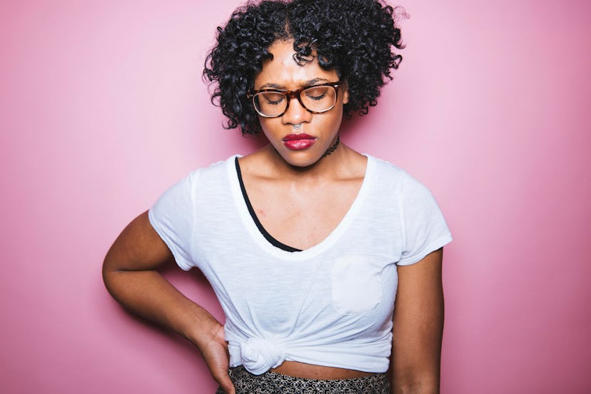 A curly-haired woman in a white shirt looking down and feeling ill due to Lyme disease