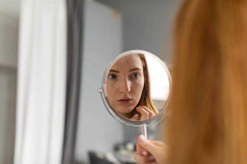 A girl looking her face in the mirror because of having skin problems