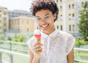 A curly-haired woman in a white lace top holding an ice-cream that makes her happy