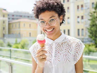 A curly-haired woman in a white lace top holding an ice-cream that makes her happy