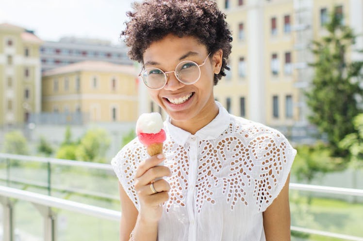 A curly-haired woman in a white lace top holding an ice-cream that makes her happy