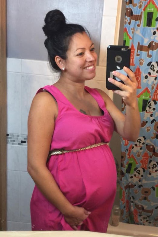 A pregnant woman wearing a pink dress takes a photograph of herself in front of the mirror
