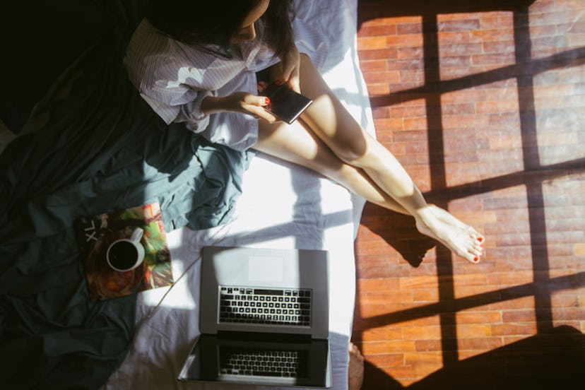 A woman sitting on her bed and on her phone taking a break and breathing