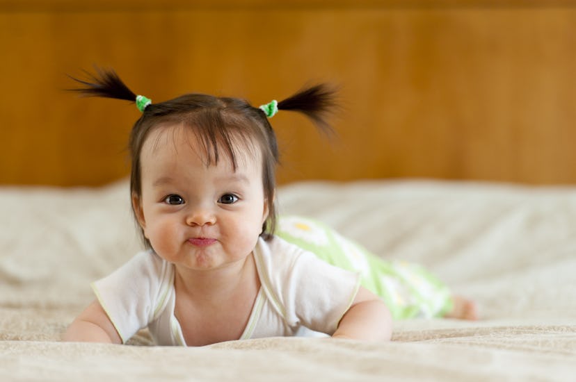 A baby with pigtails lying on the stomach and smiling.