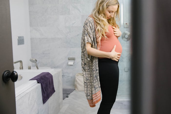 Pregnant woman standing in the bathroom while her boobs ache