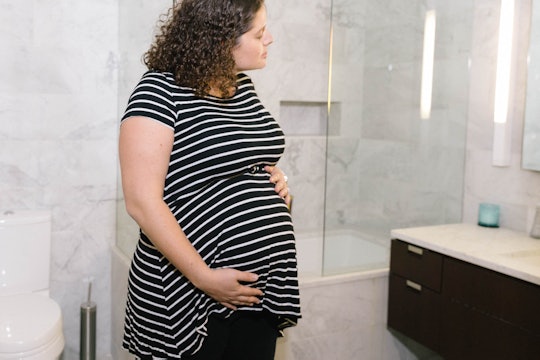 pregnant woman in black and white striped top holding belly looking at herself in the mirror