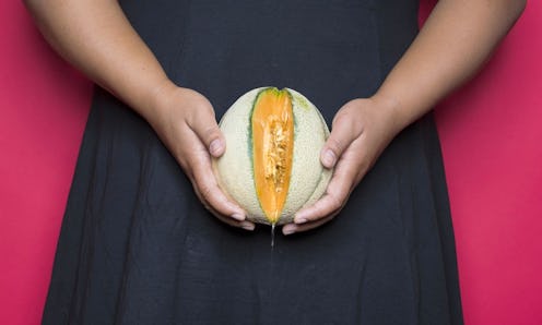 A woman in black dress holding a melon over her vagina body part