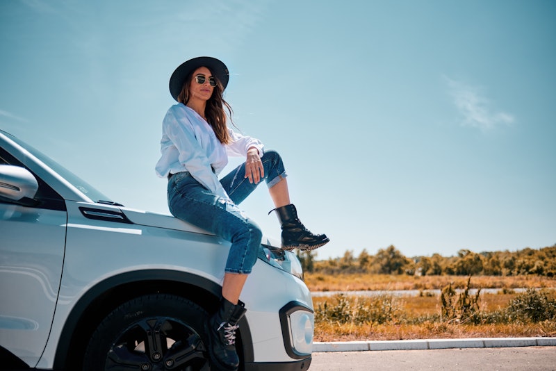 A woman sitting on a car as a spring breaker on a road trip