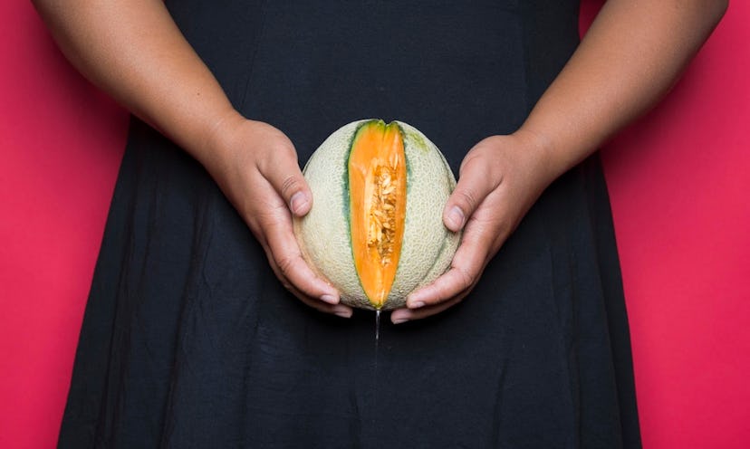 A woman in a black dress holding a melon with one slice cut out in front of her private parts