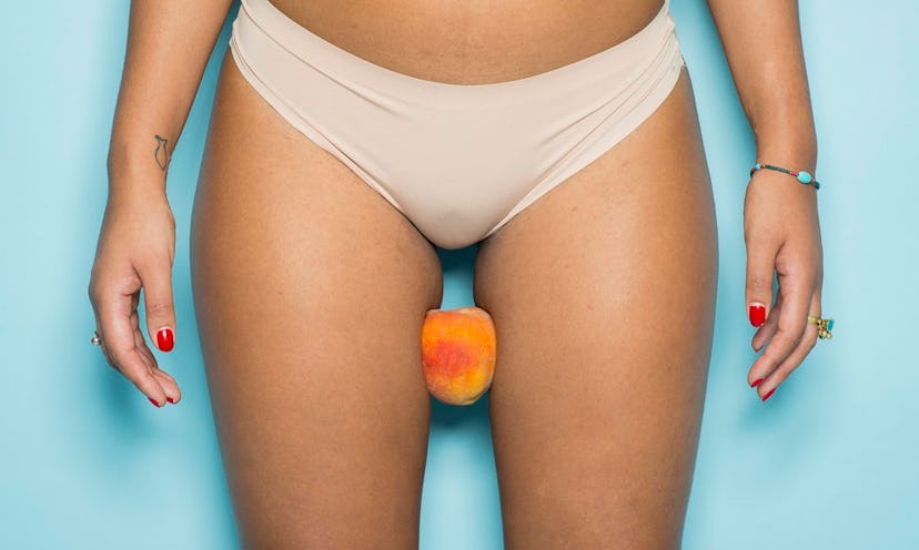 A woman in beige panties holding a peach between her thighs