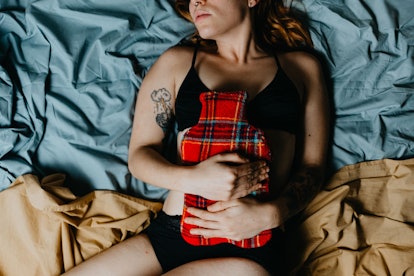 A woman with a painful period lying in bed and holding a tartan heating pad on her stomach