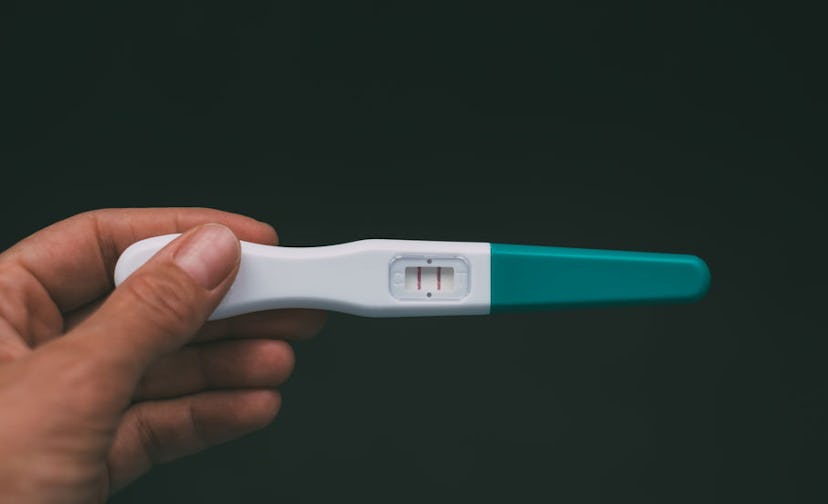 A hand holding a positive pregnancy test