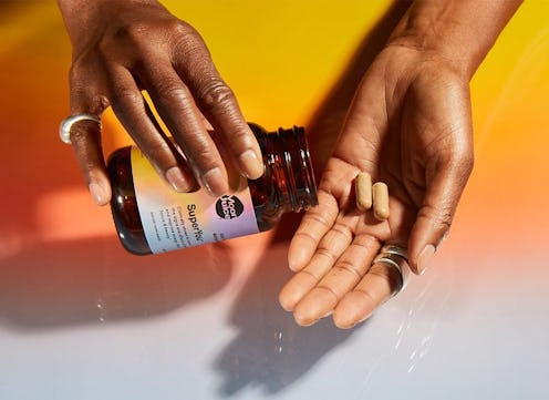 Close-up of a person taking two supplement pills from a bottle to hands.
