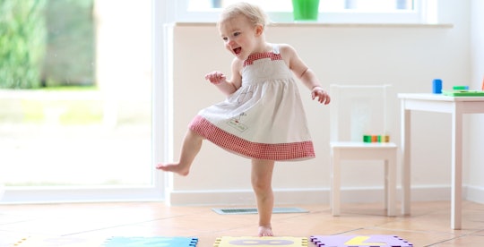 toddler in white and red dress stomping and dancing on foam tiles laughing