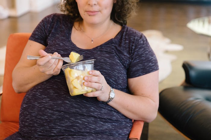 Pregnant woman sitting in chair, eating pineapple