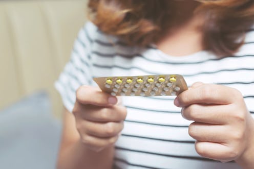 A woman in a striped blue and white shirt holding and looking at a packet of birth control tablets