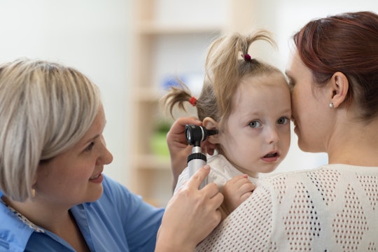 A kid in her mom's lap, getting her ear checked by a doctor due to an ear infection