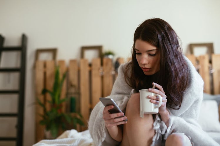 A woman on her bed drinking tea as she is nursing a cold
