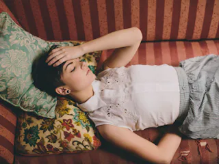 A woman with headache lying on the sofa and holding her head