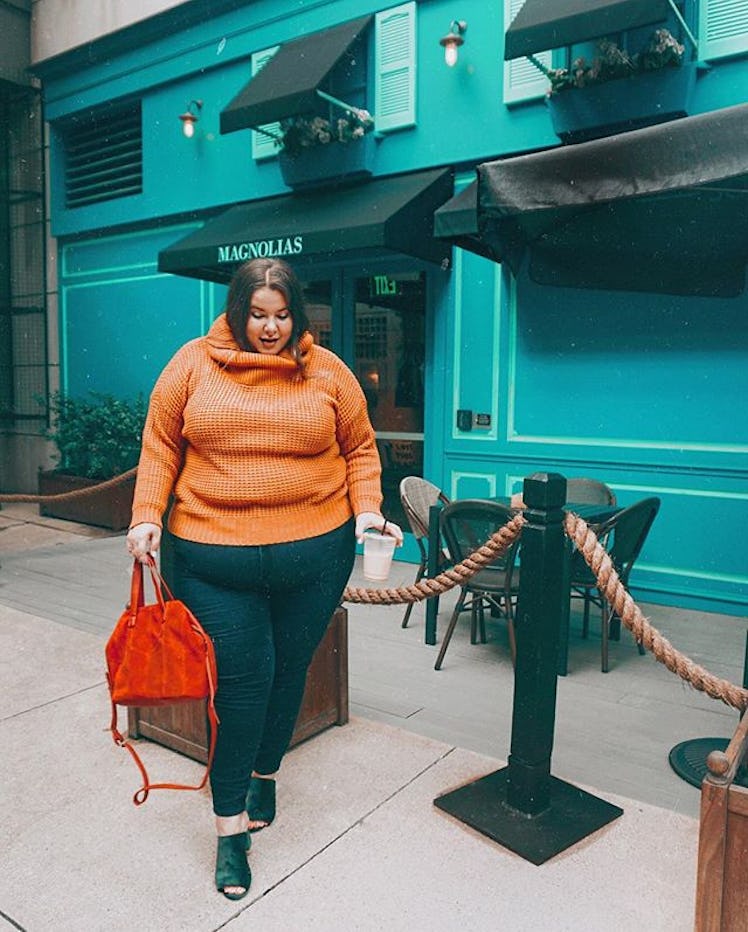 Plus-Size Influencer Natalie Hage wearing orange sweater while posing for picture. 
