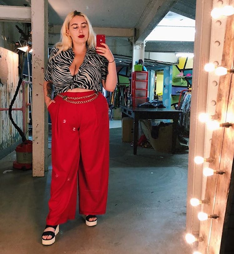 Plus-Size Influencer Gina Tonic wearing animal print crop top and high waisted red pants while takin...