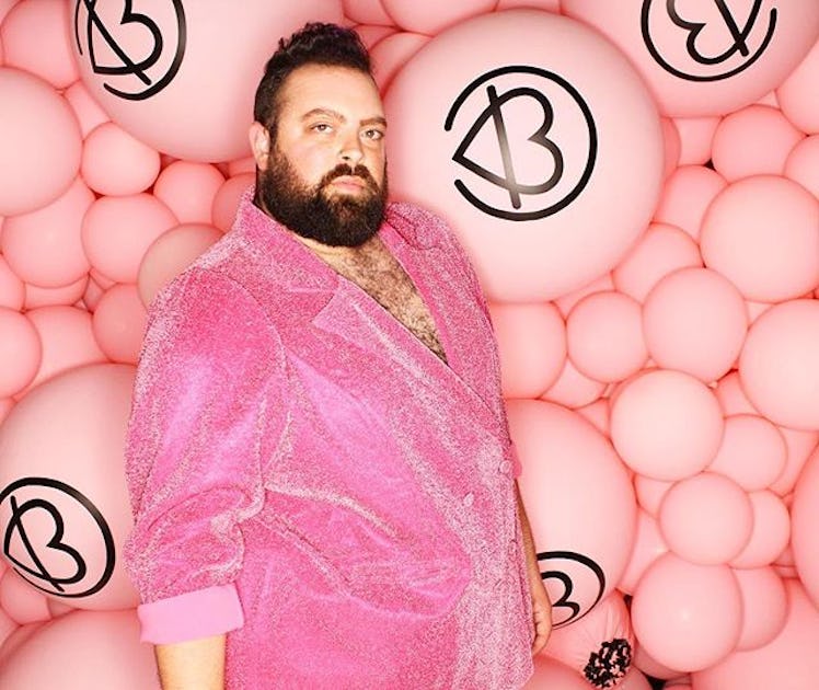 Plus-Size Influencer Troy Solomon in pink blazer posing for a picture in front of pile of pink ballo...
