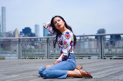 Jessica Chia, an Asian-Latinx woman sitting on a terrace floor with the NYC skyline in her backgroun...