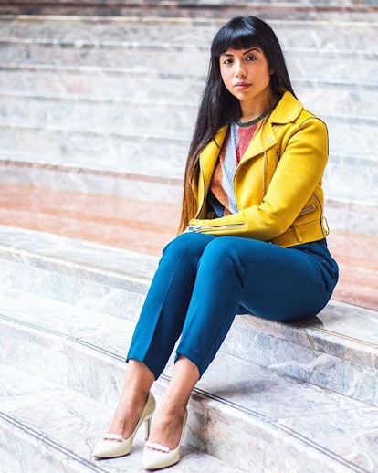 Mekita Rivas, an Asian-Latinx woman sitting on stairs, wearing a yellow leather jacket, a printed T-...