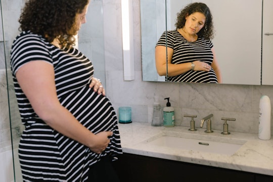 An overdue pregnant woman in a striped t-shirt checking herself out in the mirror