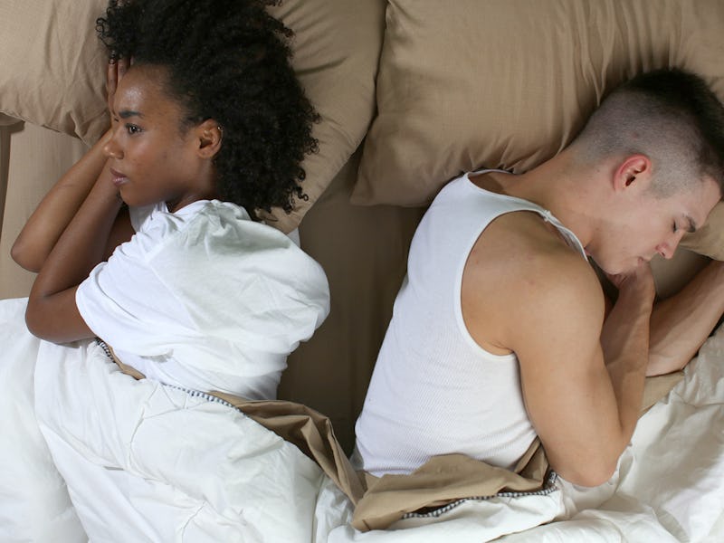 A couple lying in bed with their backs turned to each other.