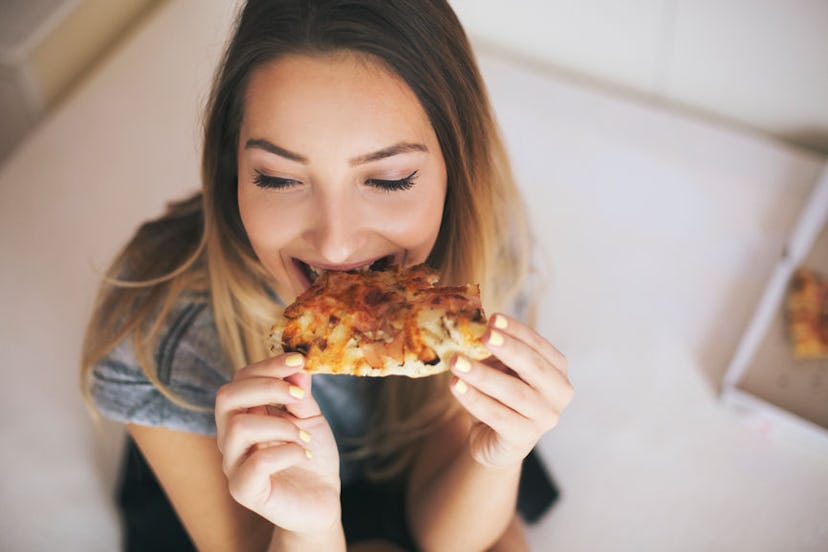 A woman eating a piece of pizza and has a headache