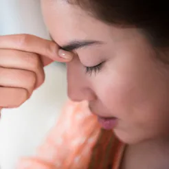 A woman experiencing a headache holding her fingers next to her forehead