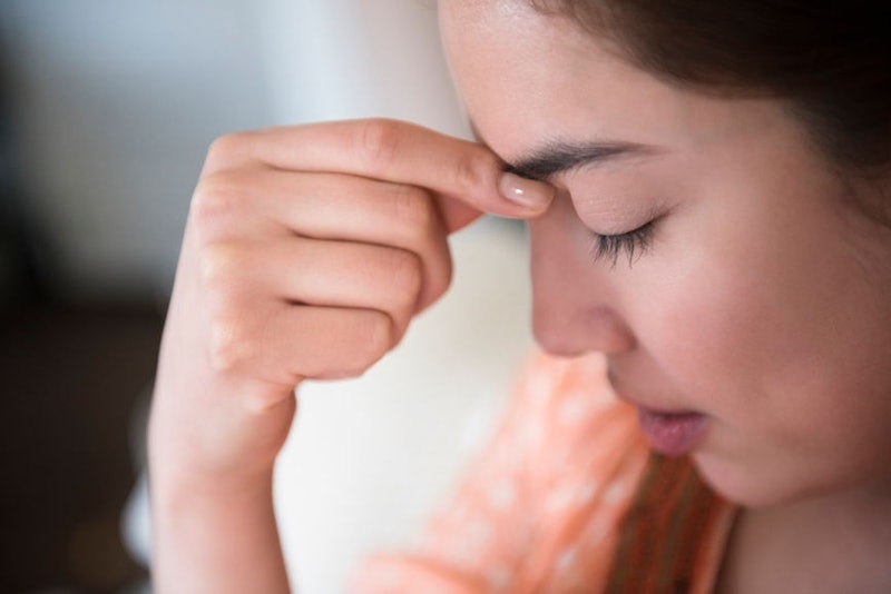 A woman experiencing a headache holding her fingers next to her forehead