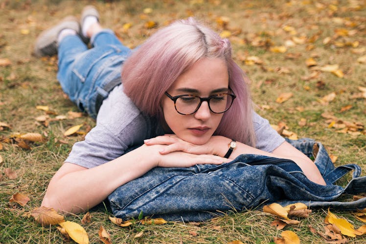 Young pink-haired girl lying on the ground, leaning her head on a backpack.