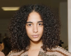 A model with curly black hair wears a patterened brown top after using gommage on her skin