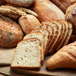 A variety of different loaves of bread piled on to each other over a wooden cutting board