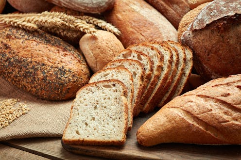 A variety of different loaves of bread piled on to each other over a wooden cutting board